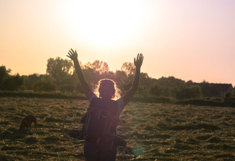 Rear view of mid adult woman with arms raised on field during sunset