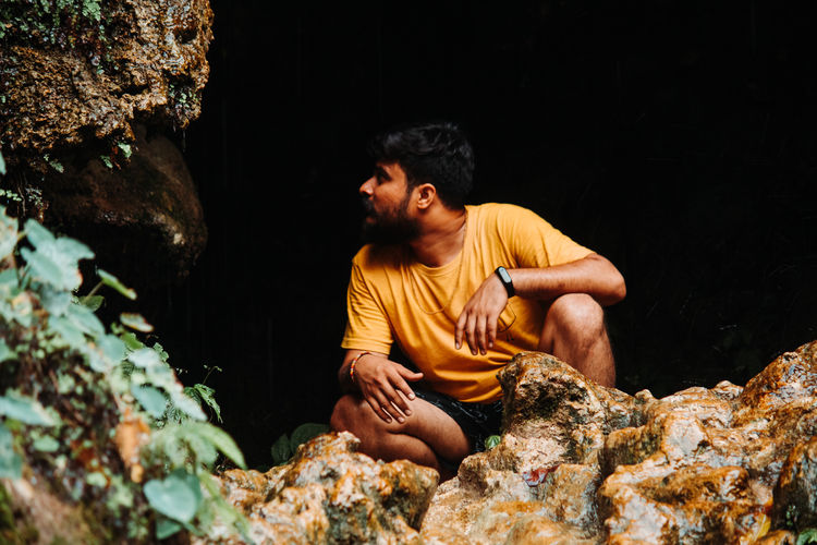 Man looking away while crouching on rock