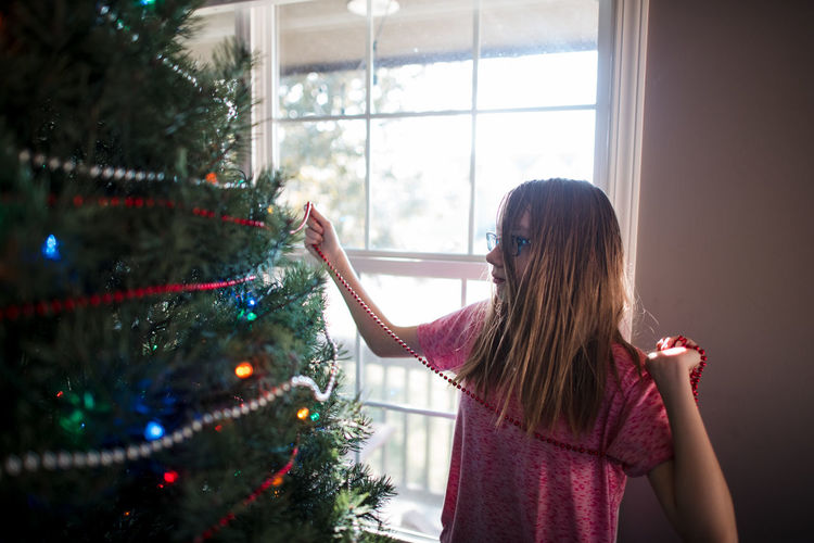Pre teen girl decorating christmas tree at home
