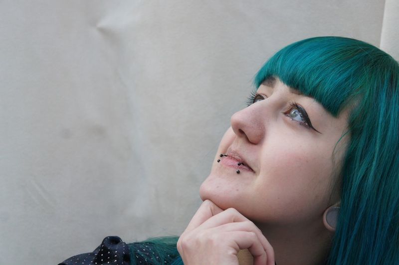 Close-up of thoughtful young woman with green hair against wall