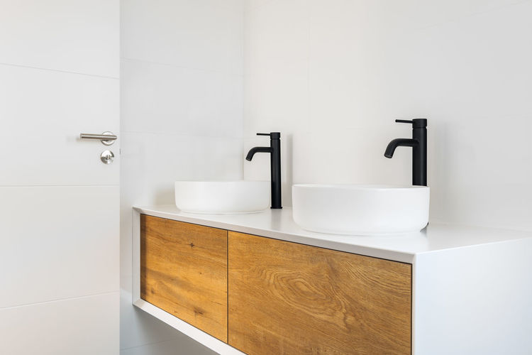 White tiled bathroom with two washbasins and black faucets.