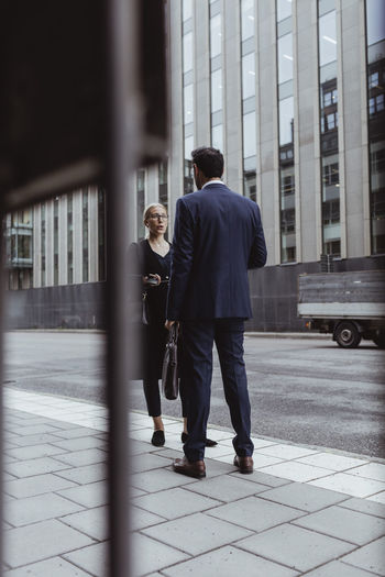 Full length of entrepreneur with bag talking to male coworker in city