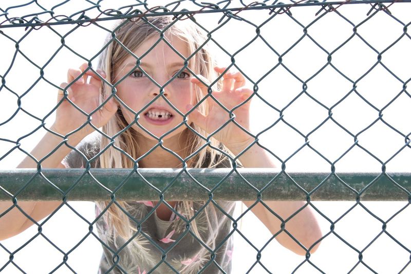 Portrait of girl making face seen through chainlink fence