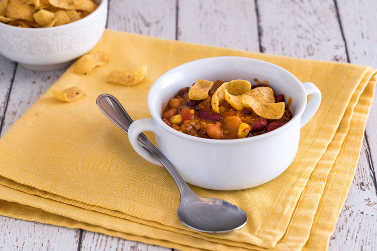 A bowl of chili con carne topped with corn chips, ready for eating.