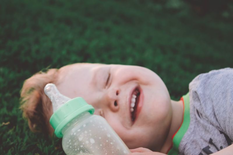 Smiling boy with milk bottle lying on field