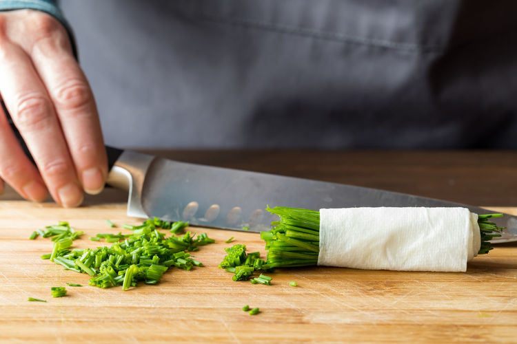 A hand holding a sharp knife in behind a pile of freshly chopped chives.