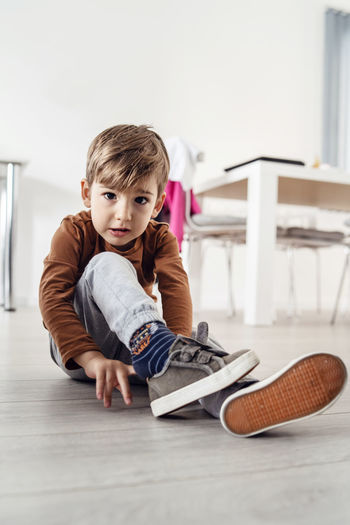 Portrait of cute boy wearing shoes while sitting on floor at home