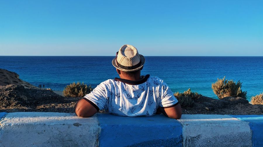 Man sitting by sea against clear sky