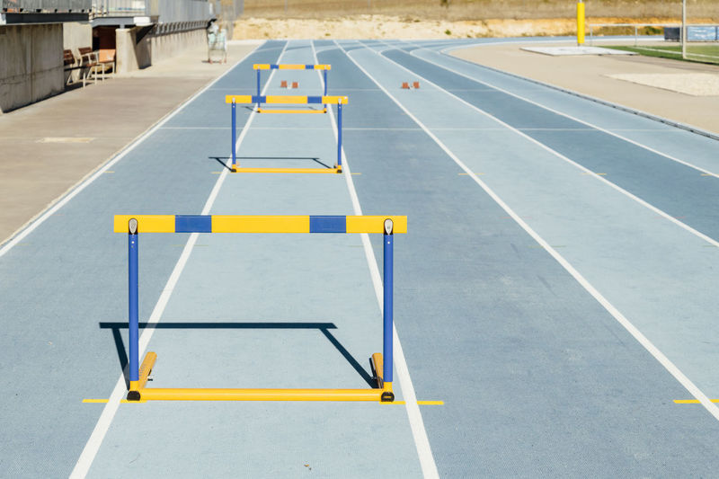 Row of colorful hurdles placed on blue racetrack during track and field workout on sunny day on stadium