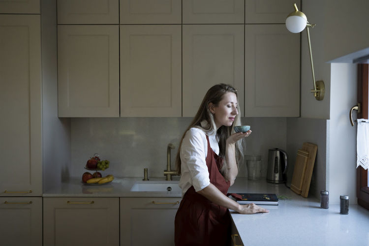 Woman with eyes closed smelling from bowl standing at kitchen counter