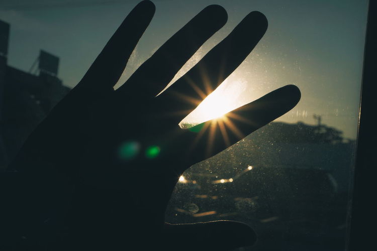 Close-up of hand against sky during sunset
