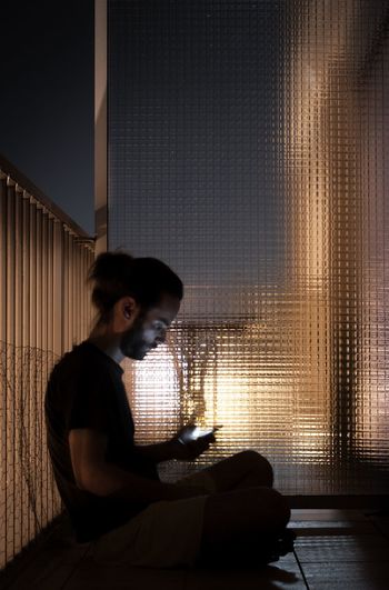 Side view of man using mobile phone in balcony at night