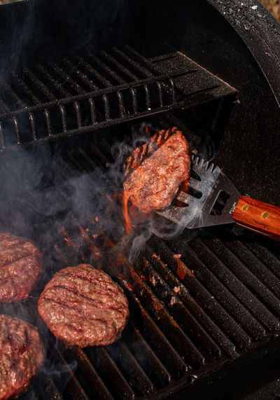 Roasted meat bbq burger patty for hamburger on metallic spatula utensils using to turn flaming grill