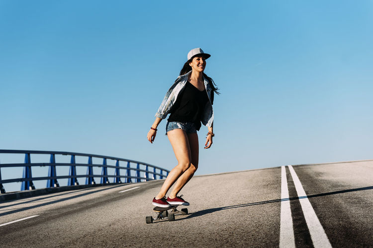 Woman skateboarding against blue sky