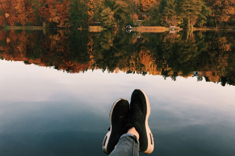 Low section of person resting by calm lake during autumn