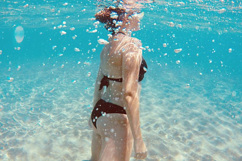 Midsection of young woman wearing bikini swimming in sea