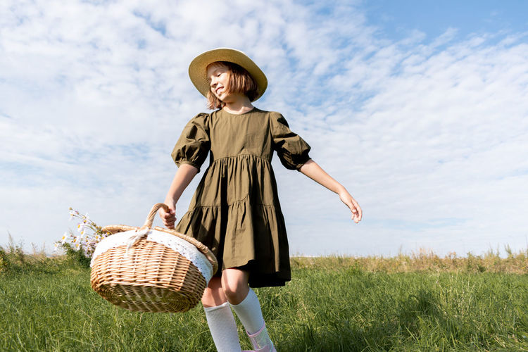 Girl in linen dress and a straw hat is dancing a flower field. wicker basket. wellness concept. 