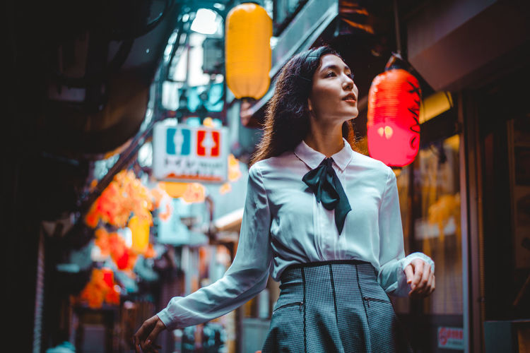 Young woman looking away while standing in city