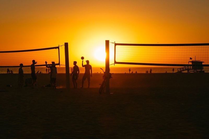 Silhouette people playing on beach against orange sky