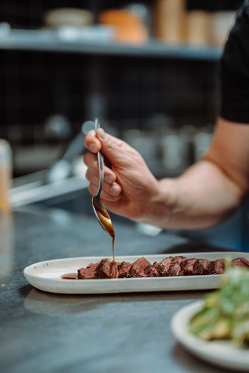 Vertical view of the unknown chief hands holding spoon and pouring sauce on beef