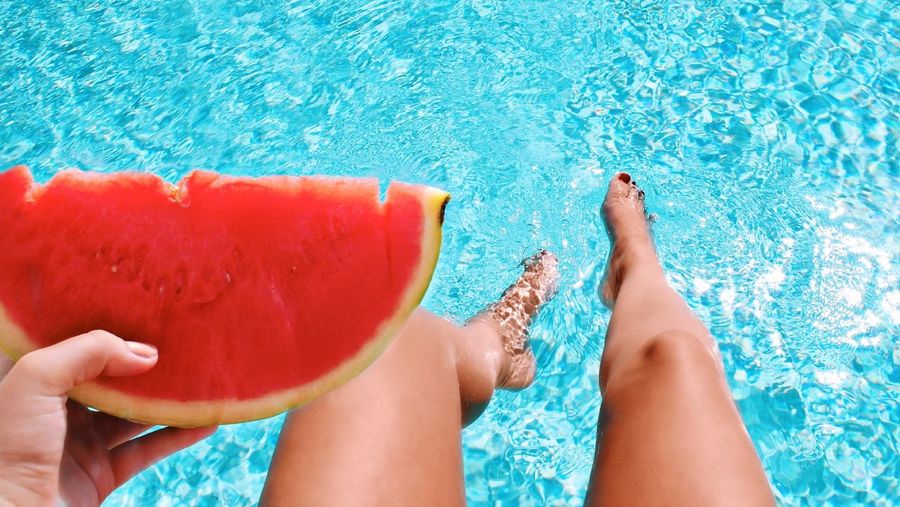 Low section of woman holding water melon in swimming pool