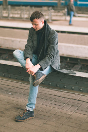 Full length of young man sitting at railroad station