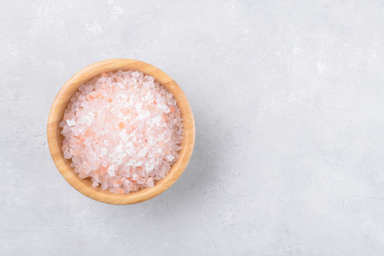 Pink himalayan salt in a wooden bowl on a light grey background, top view, flat lay, view from above