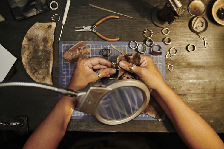 Hands of craftswoman polishing golden ring with sand paper on workbench