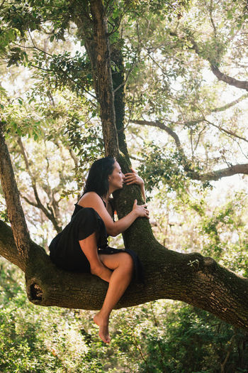 Side view of woman sitting on tree trunk