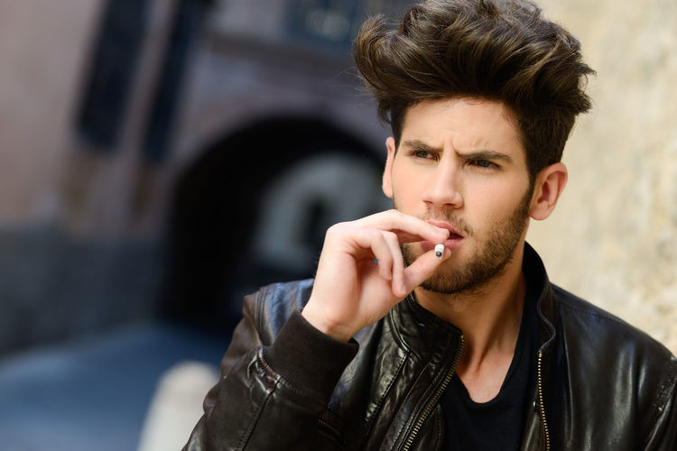 Close-up of young man smoking cigarette while standing outdoors