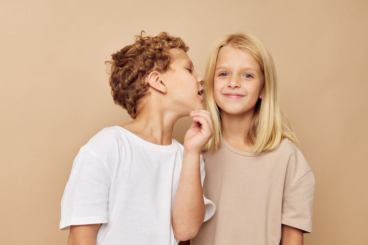 Brother whispering in sisters ears against beige background