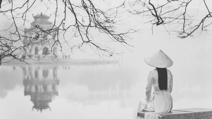 Rear view of woman wearing traditional hat while sitting by hoan kiem lake