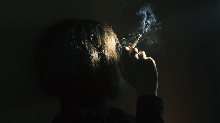 Rear view of man smoking against black background