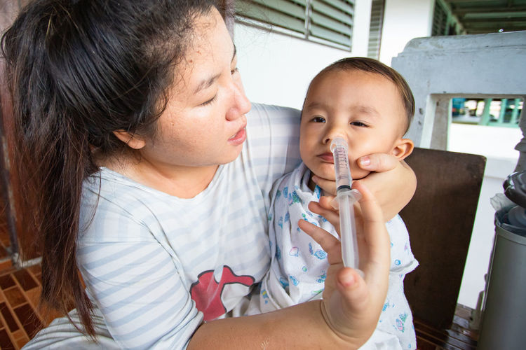 Mother inserting medicine to son through nose at home