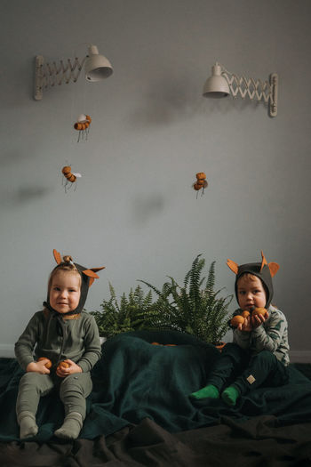 Toddler twins in funny dino costumes sitting with eggs in hands