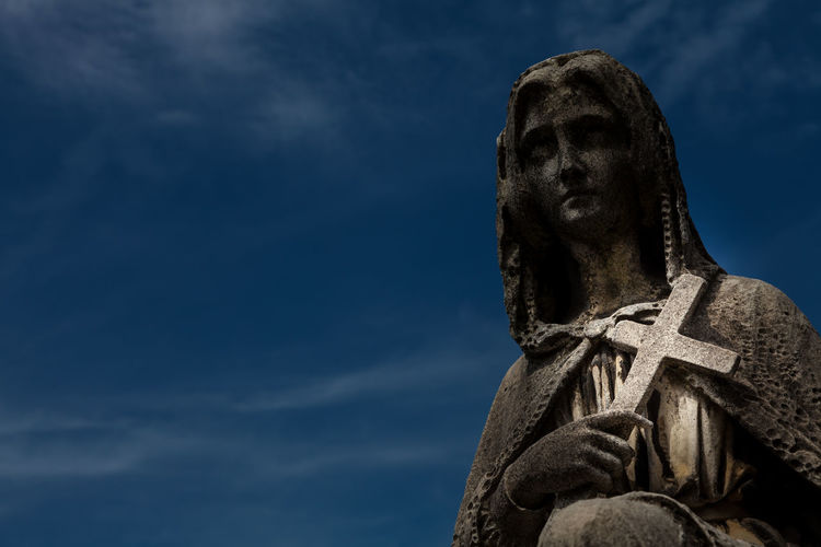 Low angle view of virgin mary statue with cross against blue sky