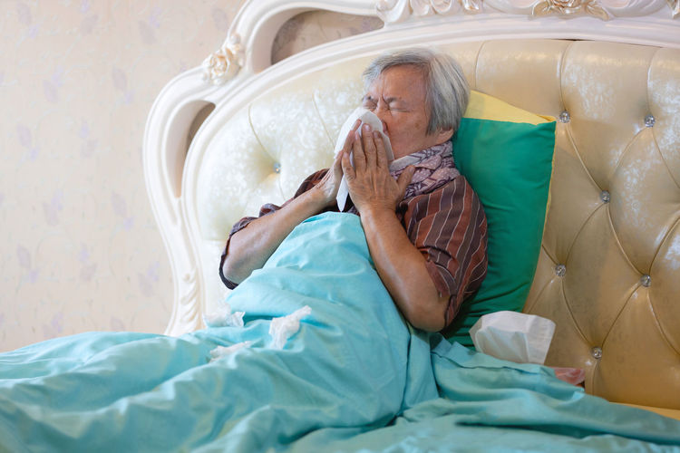 Senior woman sneezing while resting at home