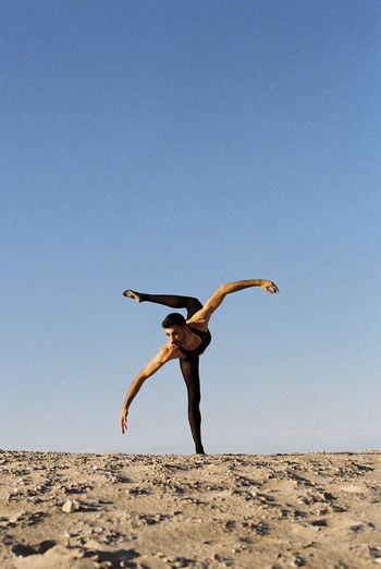 Low angle view of woman jumping against clear sky