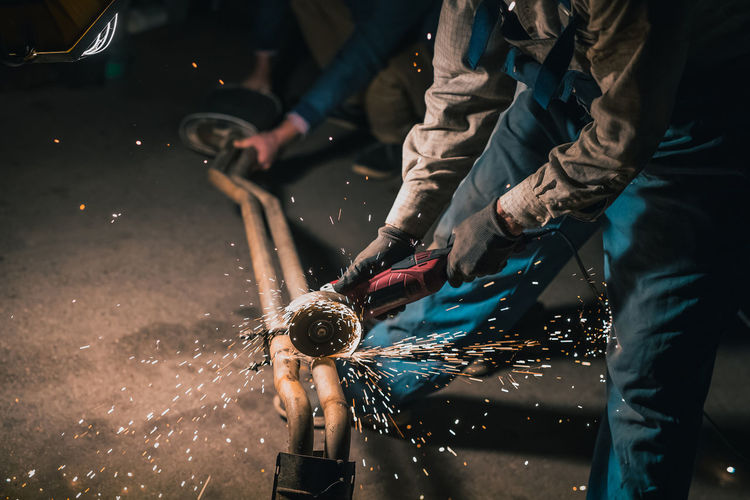 Low section of men using circular saw on metal in workshop