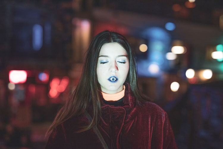 Young woman carrying artificial eye in mouth at night