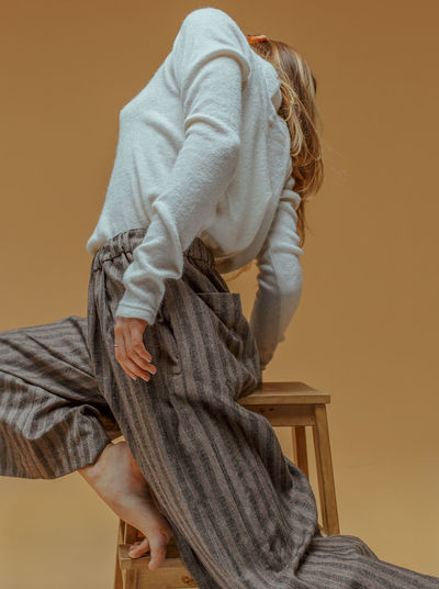 Low angle view of woman standing on stool against yellow background