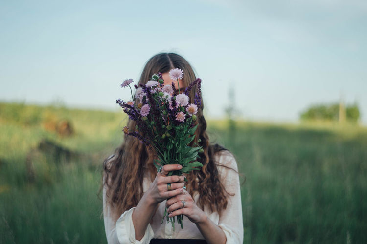 Portrait of young woman holding flower on field