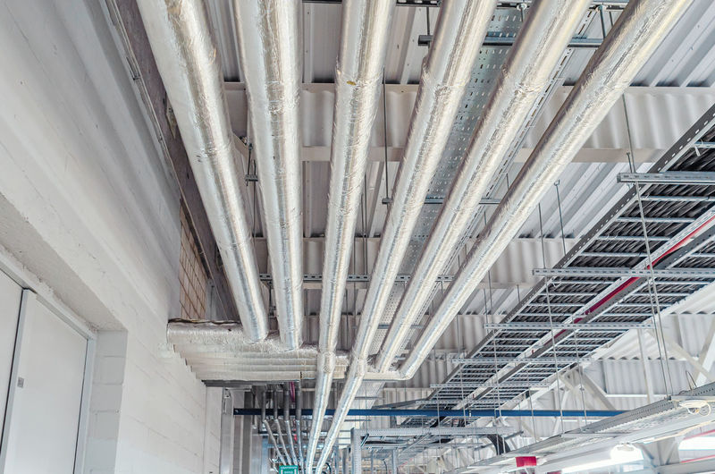 Metal pipes mounted under ceiling are covered with thermal insulation at modern production plant