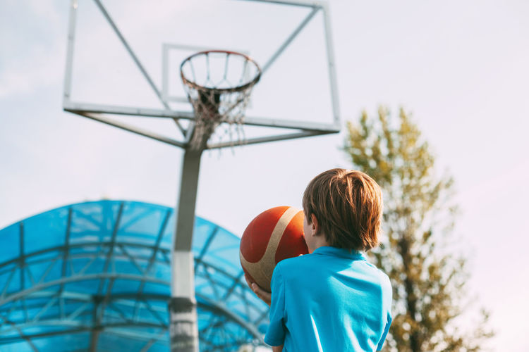A boy in a blue sports uniform is preparing to throw a basketball into the basket. 