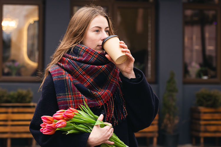 Stylish young woman with tulips drink coffee outdoors, lifestyle portrait.