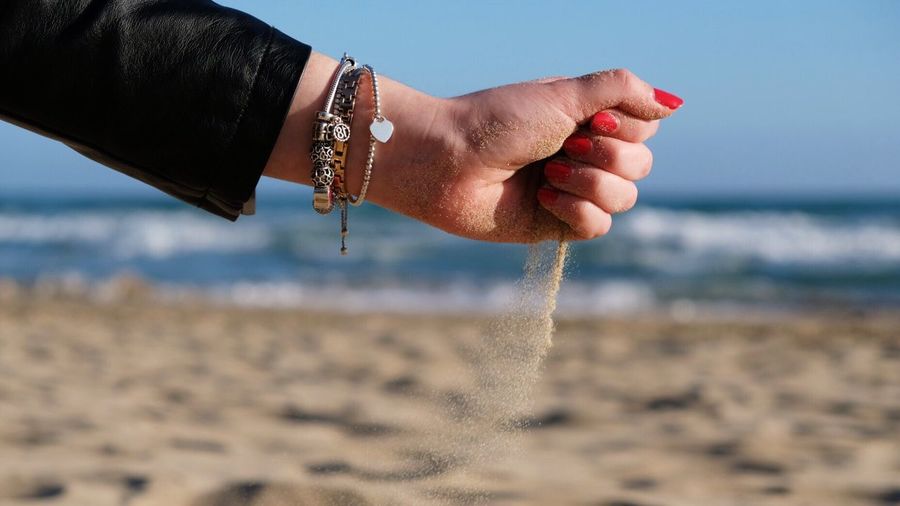 Close-up of hand holding sand on beach against sky