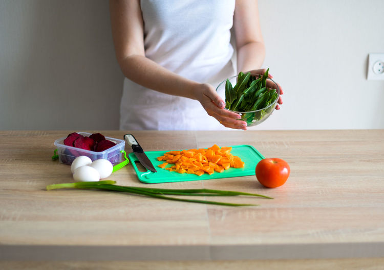 Midsection of woman holding vegetables on cutting board at home
