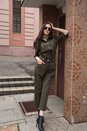 Full length front view portrait of tall slim brunette in green suit in urban setting, fashion  