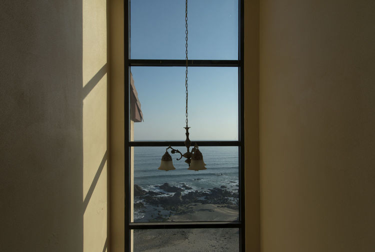 Pendant light hanging by glass window at home with sea in background