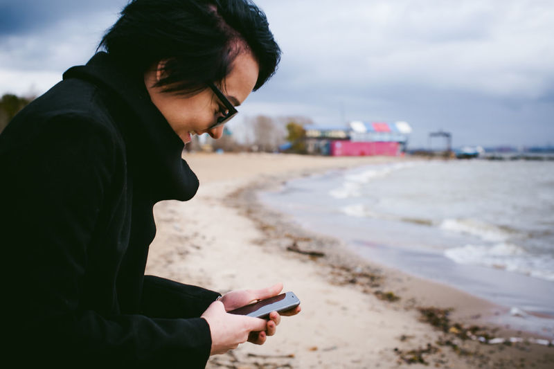 Woman using mobile phone at beach against sky